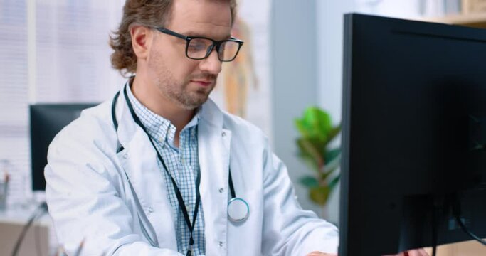 Close up of Caucasian male professional doctor specialist typing on computer keyboard browsing online at work while sitting in clinic office at workplace, general practitioner tapping on computer
