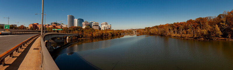 An autumn landscape panorama of Potomac river Theodore Roosevelt Island (left) and downtown Arlington Virginia. Image was taken from the Theodore Roosevelt bridge connecting DC and VA. - obrazy, fototapety, plakaty