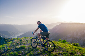 Fototapeta premium Adventurous Cyclist riding his mountain bike at the edge of a cliff, on rocky terrain while wearing no safety equipment.Amazing top view.