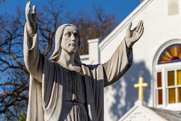 Obraz premium Rockville, MD, USA 11-16-2020: Statue of Jesus Christ with his arms open in the air as if he is talking to an audience or praying to god located in 19th century Saint Mary's Church with golden cross