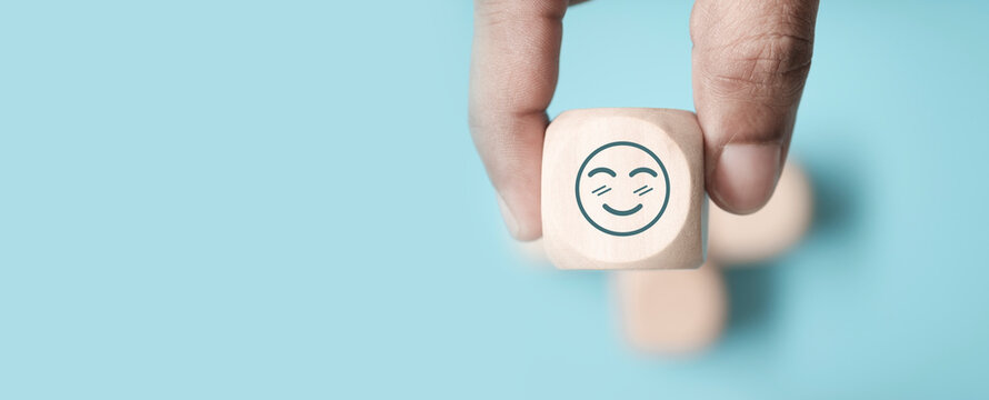 world mental health day concept or feedback rating and positive customer review, Businessman hand holding smile face, wood cube with happiness face icon on blue background