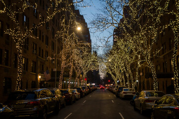 New york city street and brownstone buildings with trees covered in Christmas white lights one point perspective car dusk or early morning