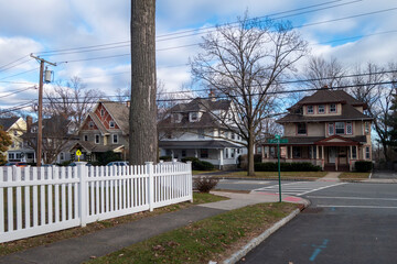 white picket fence street and sidewalk of suburban homes with leafless late fall winter season trees