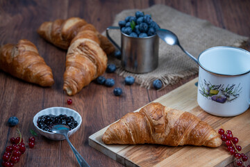 Freshly baked croissants with berries, jam on dark background, selective focus
