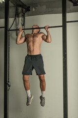 Fototapeta premium Handsome bodybuilder doing pull-ups on horizontal bar in a indoors modern gym.