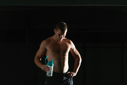 Dark contrast picture of handsome young bodybuilder drinking water from a bottle and taking a break from exercising