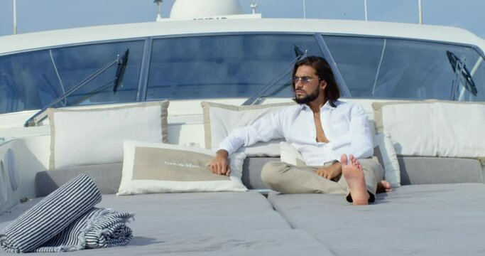 Handsome Man With Long Brown Hair And Glasses Lies On A Sofa In A Boat Under The Blue Sky - Cinematic Scene With RED Camera 4K