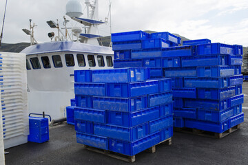 Plastic fish boxes lying on the ground by the Scottish seaside, with fishermen's boats in the...
