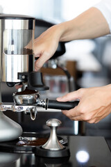 close up photo of male hands holding a metal tamper and a portafilter with coffee in a coffee shop. A man barista preparing for pressing ground coffee for brewing espresso or americano in a cafe.