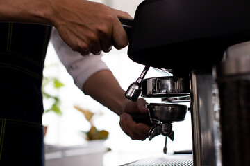 Image is portrait. Asian young man smile using a coffee machine. Rinse the coffee with warm water. Asia man preparing for pressing ground coffee for brewing espresso or americano in a cafe.