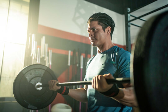 Caucasian Young Man Using Barbell For Weight Training Exercise In Gym.