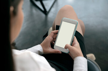 Cropped shot of young woman hands using smartphone while sitting at office, blank screen for graphic design.