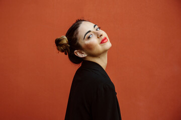 Portrait of a spanish woman, smiling, looking at the camera, with a red wall of the street on the background. Spain, young women and fashion concept. Copyspace © jesus