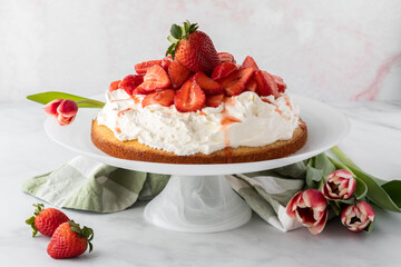 Close up of a whole strawberry shortcake on a cake stand with tulips to the side. A spring food concept.