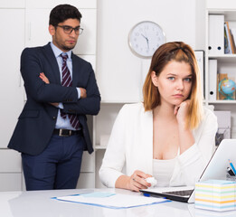 Frustrated business woman sitting at office desk on background with angry chief