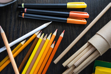 Student's stationery - color crayons, pencils, ballpoint pens for drawing class flat on brown wood texture background. Shade of yellow tone. Creative and imagination equipment for elementary design.