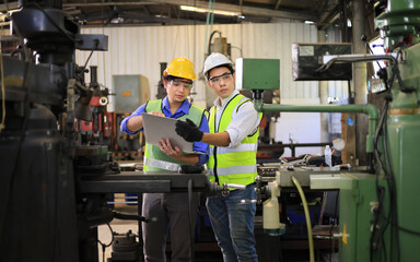Asian engineering manager and mechanic worker in safety hard hat and reflective cloth using lathe...