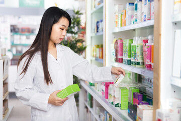 Portrait of confident chinese female pharmacist is standing with medicines in modern pharmacy