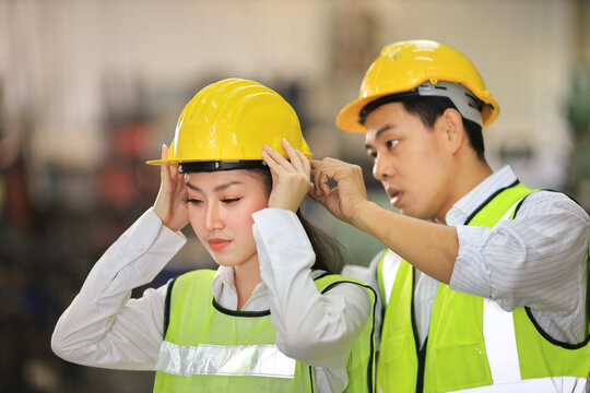 Industrial workers helping each other to wear hardhat while working inside the manufacturing factory to following safety regulation and avoiding harmful accident 