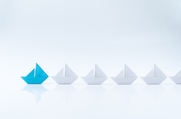 Leadership or leader concept using a blue paper ship leading among white ships