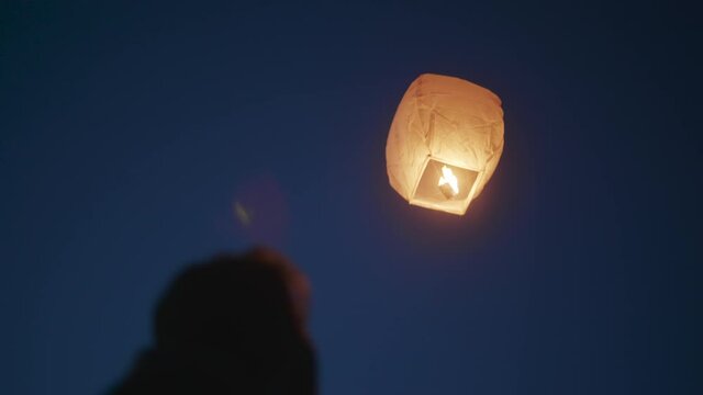 Man releases a paper sky lantern, Chinese lantern floating away at night