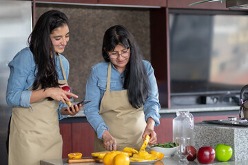 Madre e hija mexicanas cocinando en la cocina mirando la receta en el teléfono inteligente