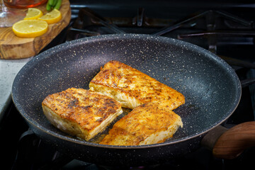Fried Halibut fish filet on pan with lemons on cutting board on background 