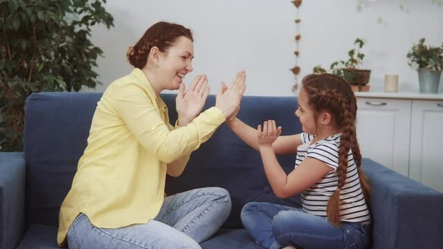mom plays with her daughter at home a clap your hands happy family kid dream stay home fun concept. mom plays with daughter on the couch sitting clap hands. young babysitter fun plays with a child