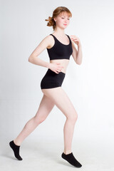 Fototapeta na wymiar A young woman in a black sports top, shorts and socks