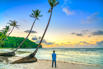 Fototapeta premium Silhouette of traveler man standing beside coconut trees watching the sunrise paradise beach on Phu Quoc island, Vietnam