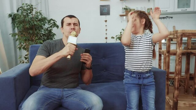 dad and daughter a sing dancing at home. stay home active leisure parents with children happy childhood concept. dad and daughter dancing sing next to the sofa with a microphone. dream kid dance