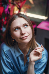 Beautiful caucasian woman in a blue shirt sits at a table in a cafe with a dreamy look