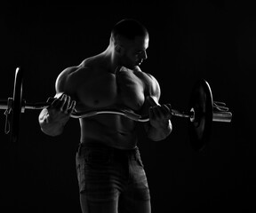 Fototapeta na wymiar Strong men athlete, bodybuilder, does exercises for biceps, looking at it during working out with barbell. Side view. Young man lifting weights. Black and white 