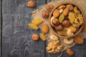 A mixture of dried fruits and nuts in a wooden bowl on a piece of burlap on a wooden table. Flat lay.