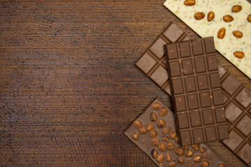 a lot of different types of chocolate lie on a brown background with nuts and chocolate flakes