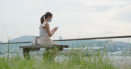 Woman wear face mask and use of mobile phone sit on the bench