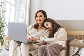 Mother middle aged woman and daughter teenager using laptop together in the light interior
