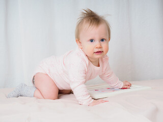 Cute gentle baby girl, 10 months old, crawling, looking surprised at the camera, close-up. Portrait of a girl in pink tones. Baby products concept. Real children's emotions