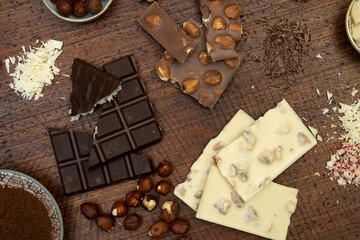 a lot of different types of chocolate lie on a brown background with nuts and chocolate flakes