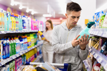 Young cheerful positive male customer making purchases in supermarket, buying household chemicals