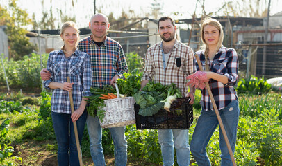 Happy family of four professional gardeners holding harvest of vegetables and greens in garden