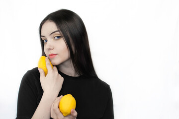 A girl with black hair holds lemons in her hands on a white background. 