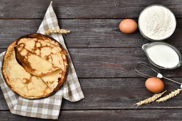 Delicious thin pancakes, a napkin and ingredients for cooking, ears of wheat on a wood table. Copy space, flat lay. Menu.