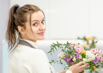 Young woman making fashion bouquet of different flowers inside her floral shop