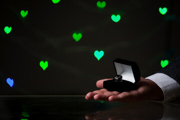 Hand holds black box with ring on background of hearts
