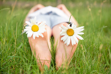 Child feet with daisy flower. Kid having fun at spring nature. Boy lying on green grass outdoors in park. Happy summer feet. Child with daisy lying in sunny meadow and relaxing in summer sunshine.