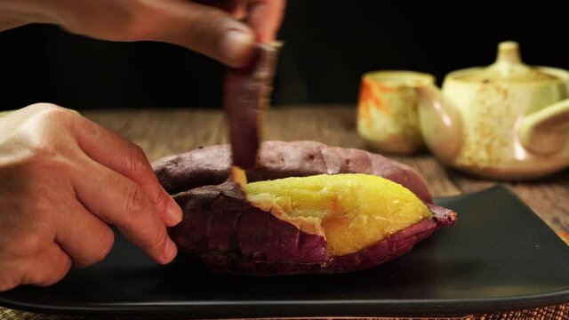 Hand open up baked sweet potato closeup, Japanese Roasted Sweet Potato on wooden table in garden.