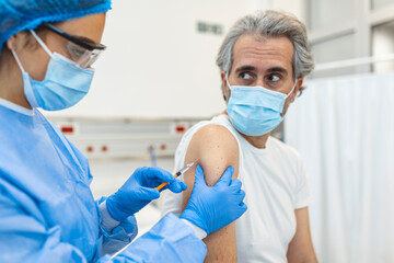 Fototapeta premium General practitioner vaccinating old patient in clinic with copy space. Doctor giving injection to senior man at hospital. Nurse holding syringe before giving Covid-19 or coronavirus vaccine.