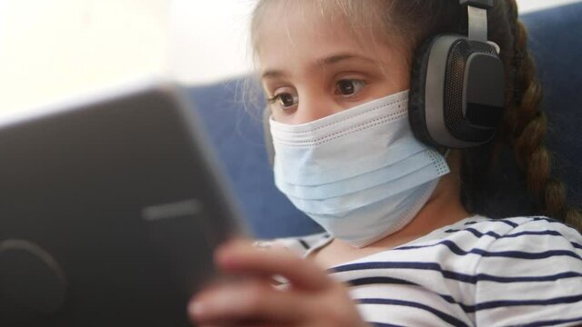 distance learning online lessons. child girl with digital tablet in mask studying remotely at home. education coronavirus online lessons lockdown concept. child learns distance school learning