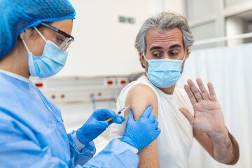 Professional doctor or nurse giving flu or COVID-19 injection to patient. Man in medical face mask getting antiviral vaccine at hospital or health center during vaccination and immunization campaign